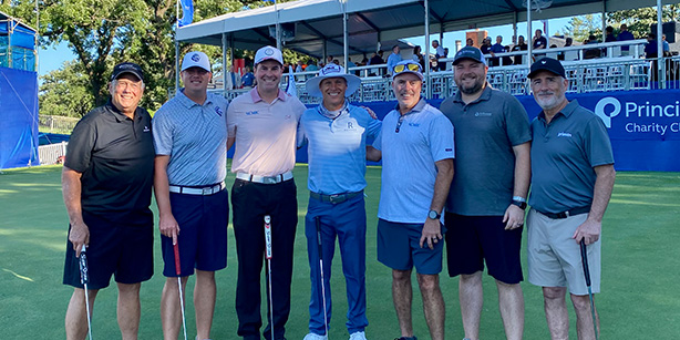 Seven men smiling for a photo on a golf course